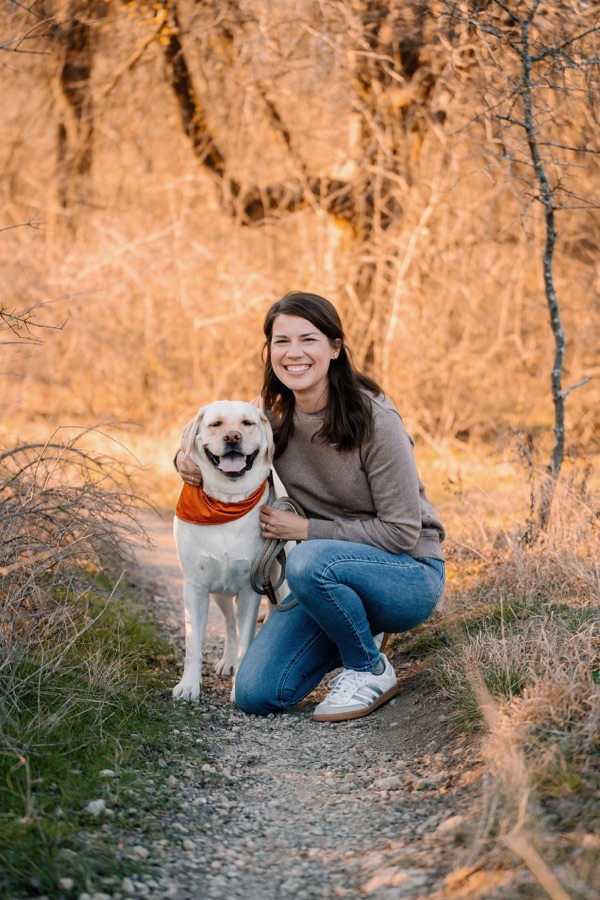 Sara smiling beside a yellow Labrador outdoors